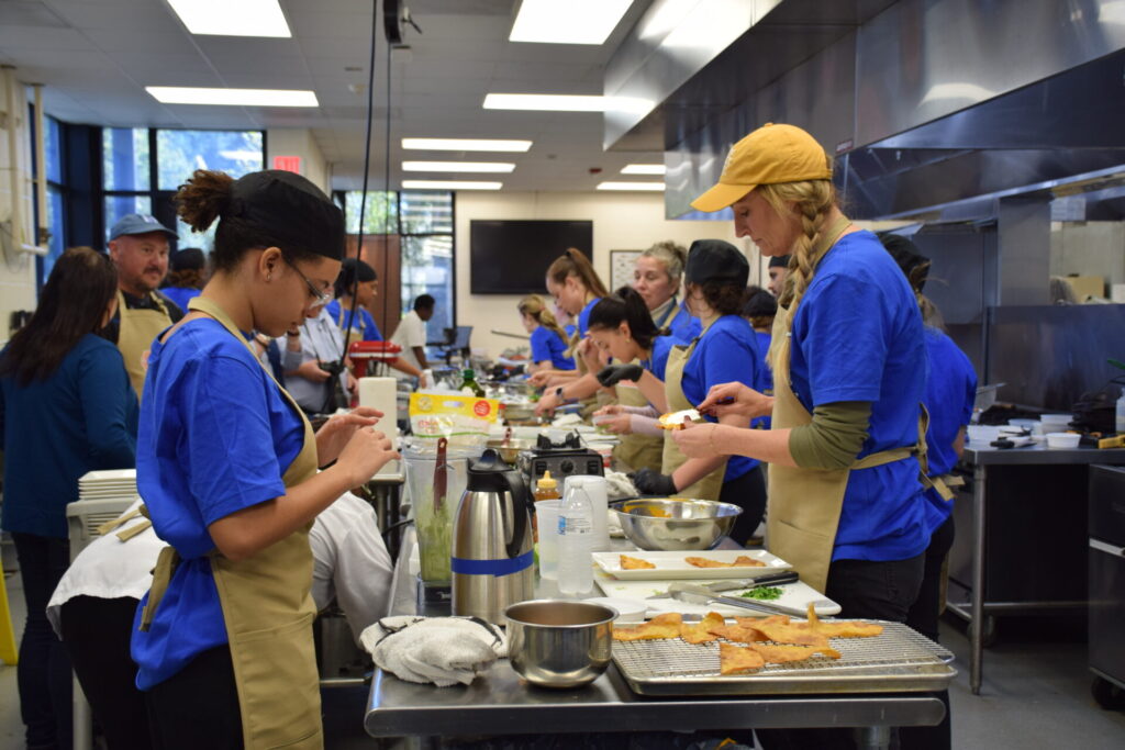 Photo of all competitors and culinary students in the kitchen.